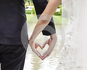 Back view of bride in white dress and groom in suit holding hands heart shape earnestly wedding theme