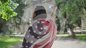 Back view of brunette woman in American flag making liberty hand gesture. Young slim lady showing freedom sign at