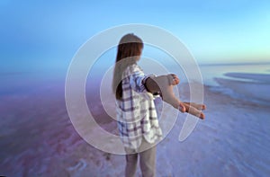 Back view brunette woman extends a hand to camera, walking by fairy beautiful evening pink lake.