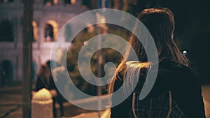 Back view of brunette woman walking late at night in Rome, Italy. Girl cross the road at crosswalk near the Colosseum.