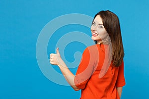 Back view brunette young woman wearing red orange dressshowing thumb up standing posing isolated over trendy blue wall