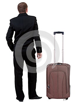 Back view of business man in black suit traveling with suitcas .
