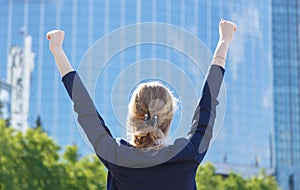 Back view of business woman facing the building with arms raised