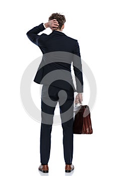 Back view of businessman holding his briefcase and scratching head