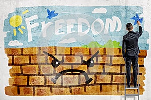 A back view of a businessman painting a beautiful sunny day on a brick wall with the word `freedom` against the sky.