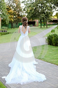 Back view of caucasian bride standing in garden and wearing long white dress.