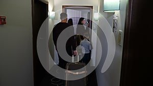 Back view of caucasian couple with 2 children and travel bag entering hotel room. Satisfied hotel guests arriving at