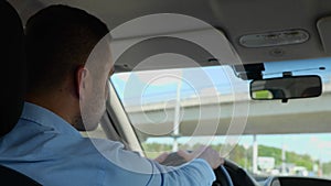 Back view of Caucasian man driving a car and looking away. Close up shot. Young adult businessman in shirt drives his