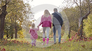 Back view of caucasian man strolling with his two daughters dressed in pink clothes in the autumn park. Happy family