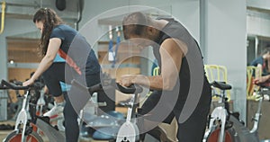 Back view of caucasian sportive people entering gym and sitting on exercise bikes. Slim athletic men and women start