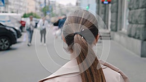 Back view of caucasian woman in jacket walking city in the downtown. Rear view of young female employee commuting to