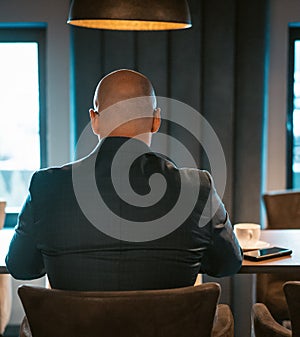 Back view of CEO businessman dressed in expensive suit sitting at the table in the modern expensive office interior