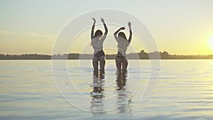 Back view of charming slim Caucasian tanned women dancing in river at sunset. Extreme wide shot of joyful young female