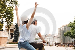 Back view of cheerful couple in helmets riding on scooter