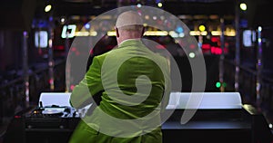 Back view of cheerful old caucasian man dancing and spinning next to music controller in night club. Elderly DJ having