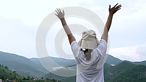 Back view of cheerful young woman  with her arms outspread on peak of mountain with sky background. Achievement and winning concep