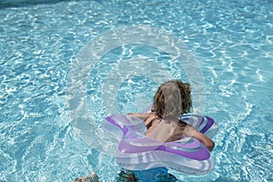 Back view of a child with a lifebuoy swimming in the pool