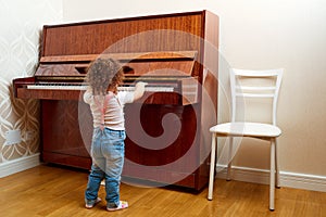 Back view. A child stands in front of the piano and plays a melody. Little pianist learning to play the piano. Baby, child