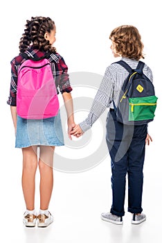 back view of classmates with backpacks holding hands photo