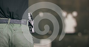 Back view close-up of a man pulling a pistol out of its holster and firing a shot at a shooting range