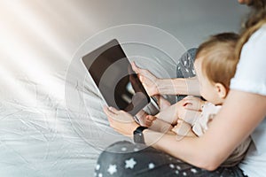 Back view.Close-up of tablet computer in hands of mother sitting with baby. Toddler girl looking at screen of smartphone
