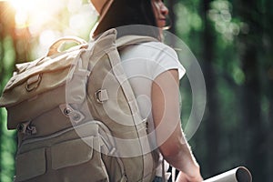 Back view of close-up traveler backpack and cute brave woman traveling alone among forest on outdoor