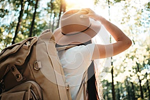 Back view of close-up traveler backpack and cute brave woman traveling alone among forest on outdoor