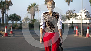 Back view of confident elegant Caucasian slim woman walking in slow motion along road construction site outdoors