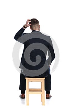 Back view of confused businessman scratching his head and sitting