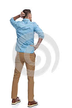 Back view of confused young man in denim shirt scratching head