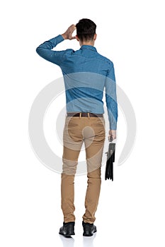 Back view of confused young man scratching head