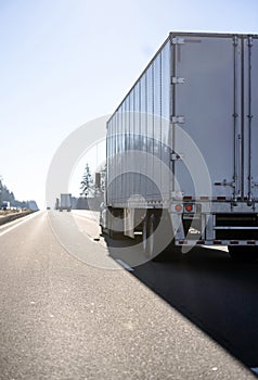 Back view of convoy of big rigs semi trucks running with semi trailers on the divided road