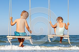 Back view couple of cute little adorable small caucasian sibling kids enjoy having fun swinging and playing at