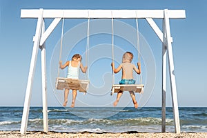 Back view couple of cute little adorable small caucasian sibling kids enjoy having fun swinging and playing at