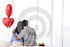 Back view of couple happy Asian lover hugging each other while sitting on white bed, romantic couple celebrate memorable