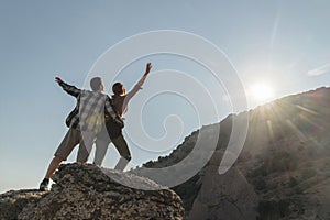 Back view of couple hikers standing on rock enjoying freedom raising hands up