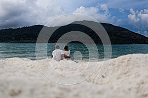 Back view couple sitting on the sandy beach