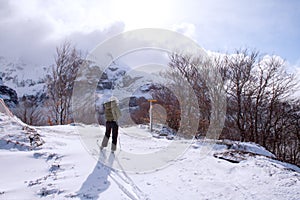 Back view of cross country female skiier in the middle of a full of snow track with trees at each side and mountains in tha backgr