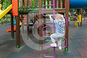 Back view cute adorable caucasian blond little toddler boy kid having fun enjoy climbing metal stairs at children modern