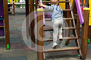 Back view cute adorable caucasian blond little toddler boy kid having fun enjoy climbing wooden stairs at children