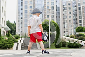 Back view of cute alone sad adorable caucasian 3-4 years blond little kid boy in stylish shorts shirt and hat hold soft