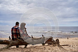 Back view of a cute couple with matching shirts sitting on a tree trunk on a sandy beach