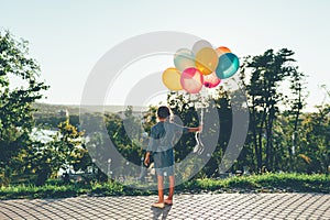 Cute girl holding colorful balloons in the city park dreaming