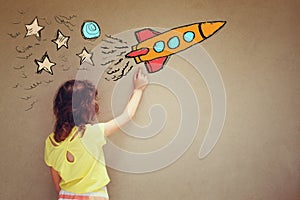 Back view of cute kid (girl) imagine space rocket with set of infographics over textured wall background photo