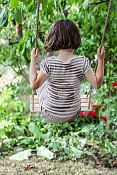 Back view of cute kid swinging to relax in summertime
