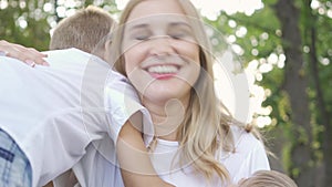 Back view of cute little girl and boy hugging mother. Woman laughing and hugging son and daughter. Happy family in park