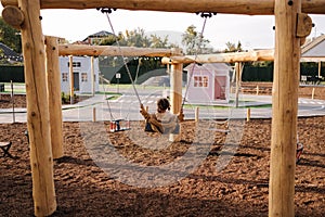 Back view of cute little girl swing on a swing in the specially designated place in the park. Softner from sawdust