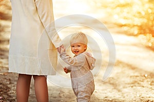 Back view on a cute little toddler boy holding his mother`s hand and smiling . Adorable child walking with his mom in