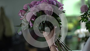 Back view of cute young woman florist wearing apron compose new bouquet.