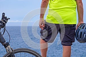 Back view of cyclist man resting at sea on the cliff after activity with his electro bike. Standing with helmet in the hand